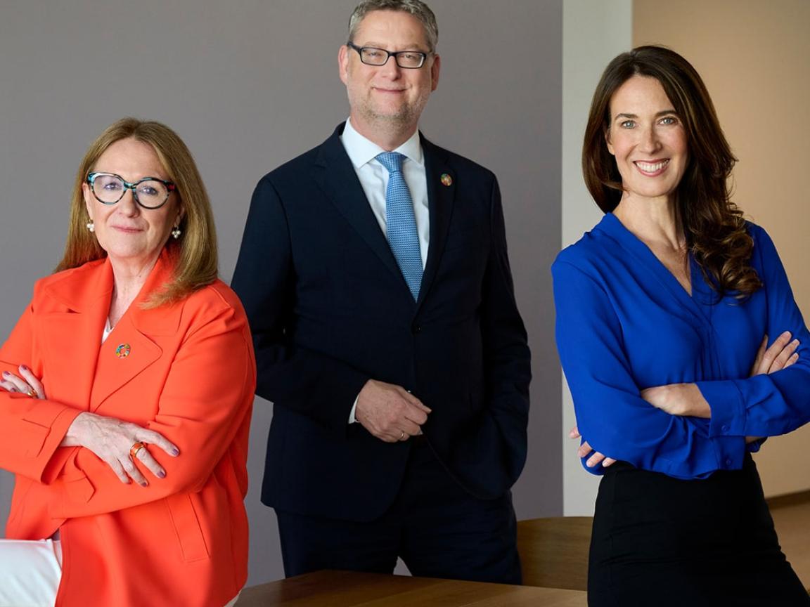 Drei Personen in professioneller Kleidung, zwei davon Frauen, in der Mitte ein Mann. 