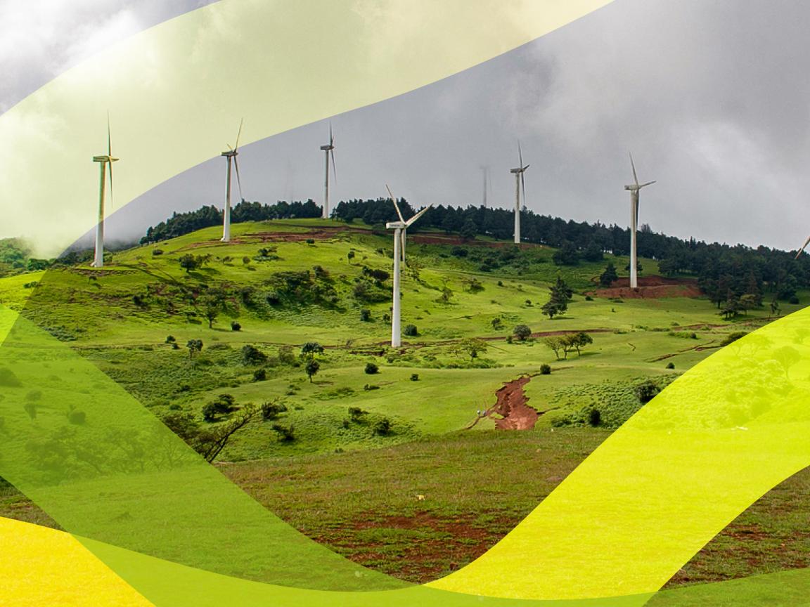 Wind turbines on a green hill under a cloudy sky.