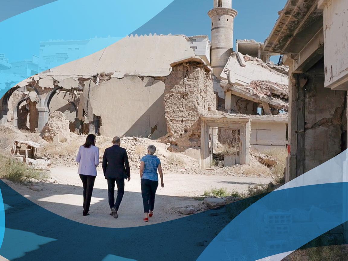 Three people walk along a street. All of the buildings are severely damaged. 