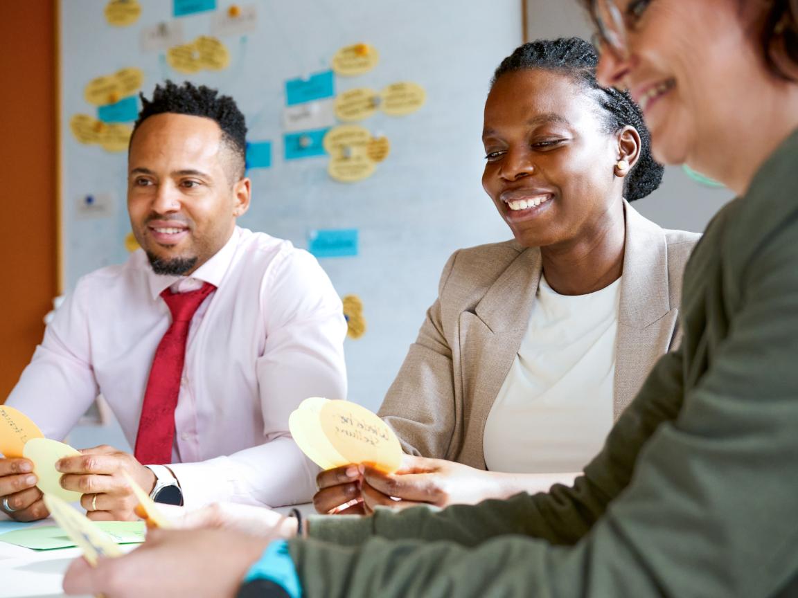 Two women and a man sit at a table, each holding some index cards.