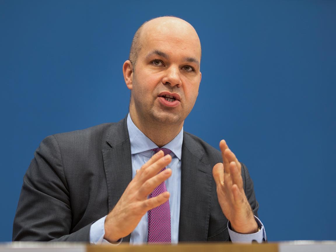 Marcel Fratzscher, in a suit and tie against a blue background, speaking and gesturing with both hands in front of him.