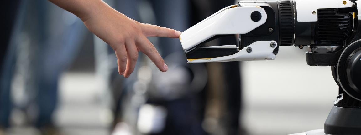 Eine menschliche Hand und eine Roboterhand berühren sich beinahe, symbolisch für die Interaktion zwischen Mensch und Technologie.