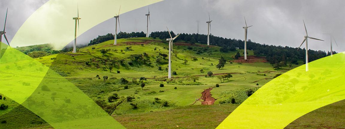 Wind turbines on a green hill under a cloudy sky.