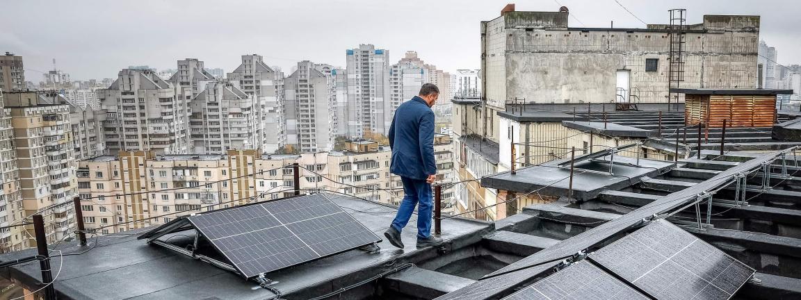 Ein Mann läuft über ein Flachdach mit installierten Solarpanels, im Hintergrund stehen viele Hochhäuser einer Stadt.