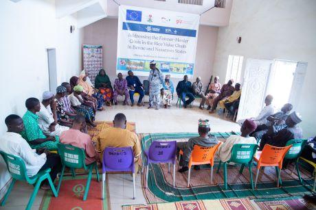 Ein Gruppe von Personen sitzen in einem Stuhlkreis, eine Person ist aufgestanden und scheint zu reden. Im Hintergrund sieht man ein großes Banner, dass den Grund des Treffens beschreibt und das GIZ Logo abzeichnet. Lesbar ist das Plakat in dem Foto nicht.