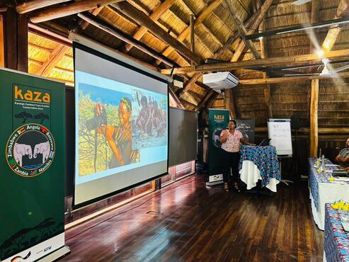 Woman on a stage talking and showing 2 pictures.