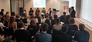 5 Personen sitzen auf Stühlen auf einer Bühne mit Publikum