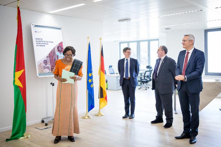 Eine Frau hält ein Papier in der Hand und steht vor 3 Männern