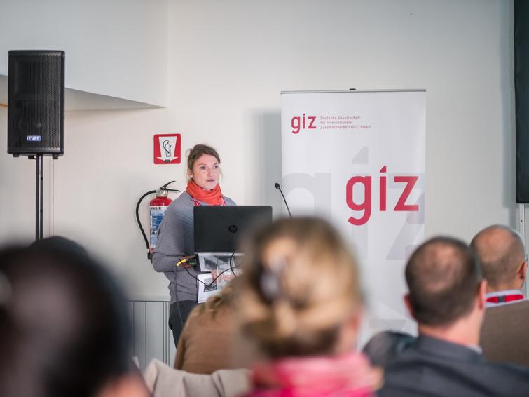 Eine Frau steht an einem Pult und redet zu einem Publikum