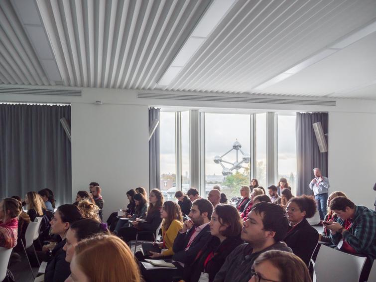 Viele Personen sitzen auf Stühlen verteilt in einem Raum