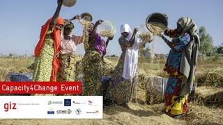 Frauen stehen in einem Feld und schütten den Inhalt ihres Eimer aus