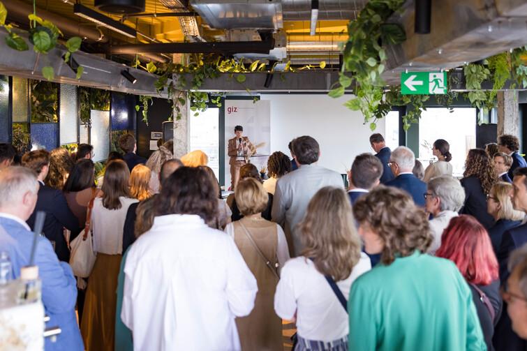 Person steht vor einem Publikum und hat ein Mikrofon in der Hand