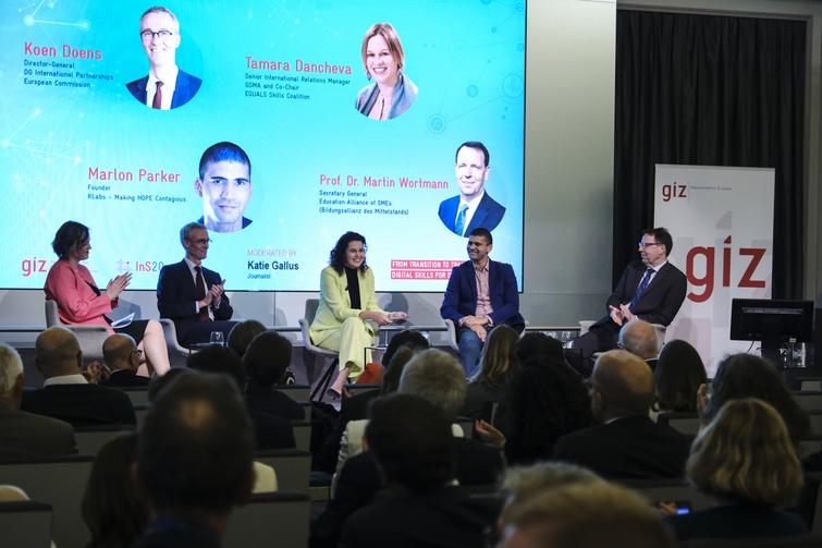 5 Personen sitzen auf Stühlen auf einer Bühne mit Publikum