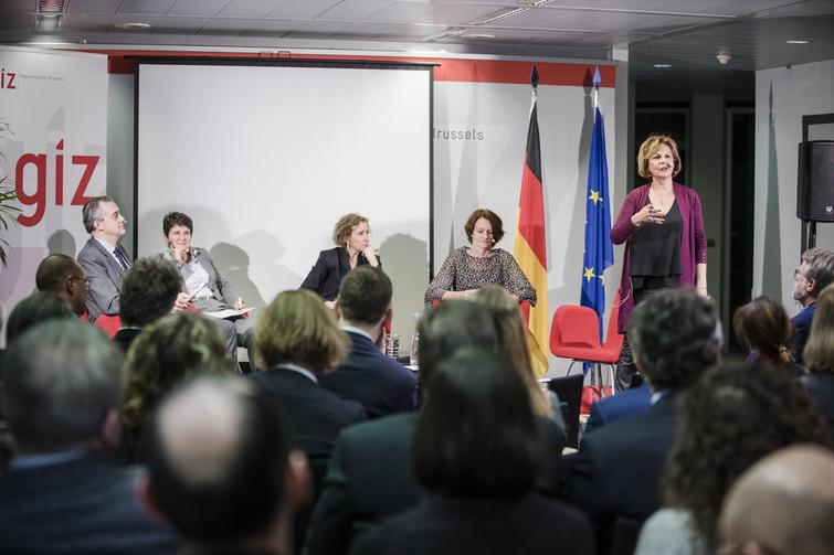 Mehrere Personen sitzen auf roten Stühlen in einem halb Kreis. Eine Frau ganz rechts steht