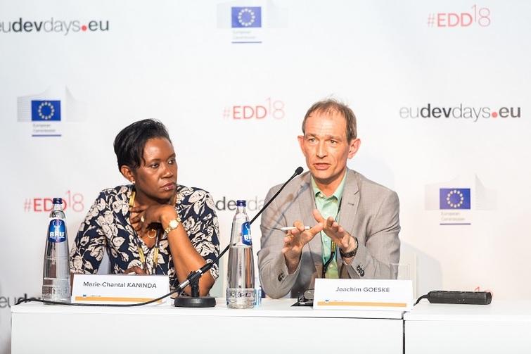 Mann redet in ein Mikrofo. Eine Frau sitzt links von ihm