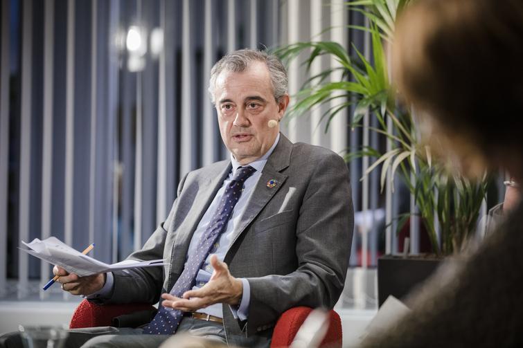 Mann sitzt in einem roten Stuhl und hält in der einen Hand Papiere und einen Stift