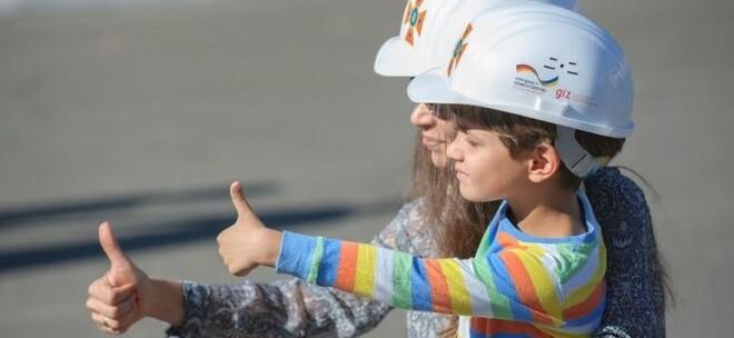Frau hält einen Jungen im Arm. Beide haben einen weißen Helm auf und zeigen den Daumen nach oben