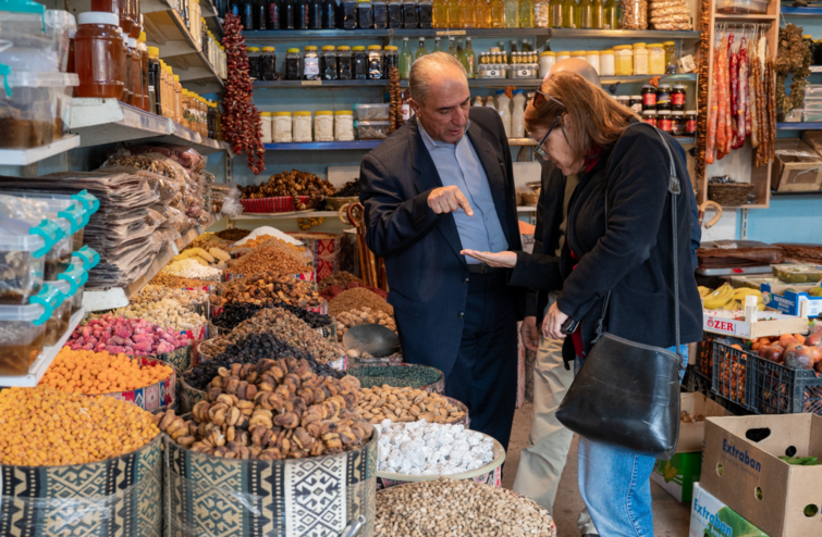 A man explaining something to a woman inside a store with nuts and dried fruit.