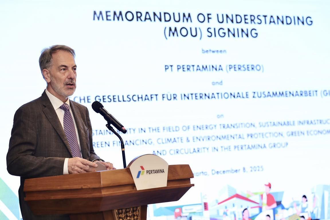 Country Director speaking at podium with the backdrop with Information on the the MoU Signing between Pertamina and GIZ