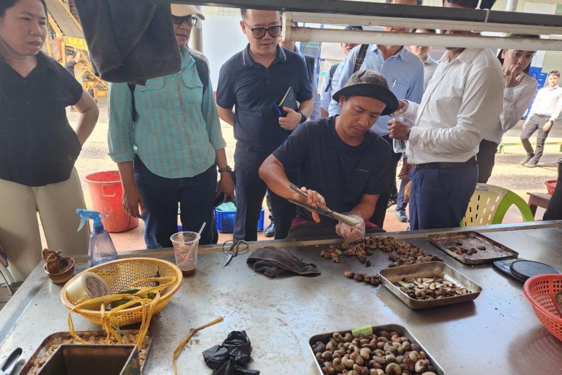 A group of people is standing behind a man sitting at a table and roasting nuts.