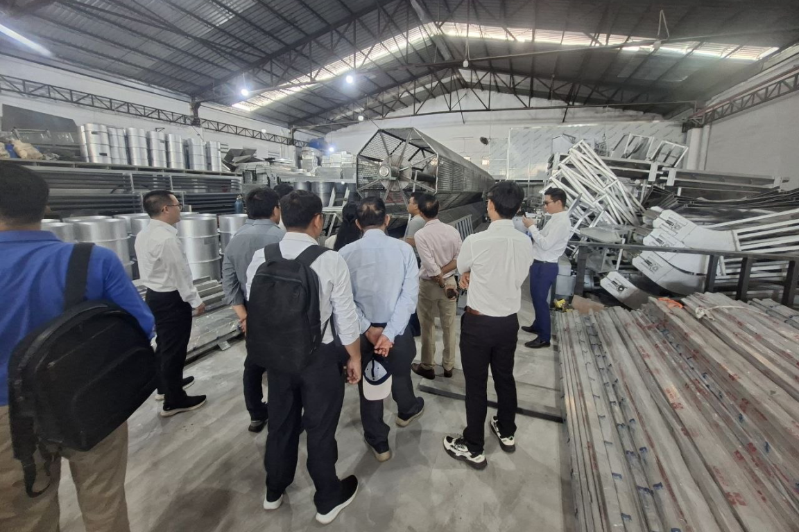 A group of men is standing in a factory hall where metal items are assembled.