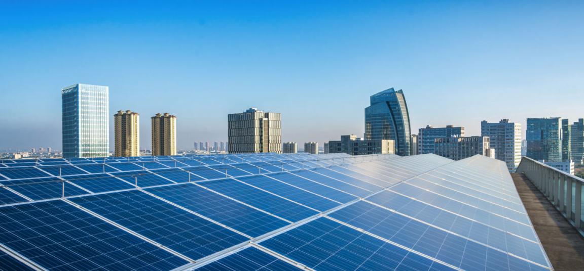 Rooftop solar photovoltaic panels installed on a modern urban building, with a city skyline in the background