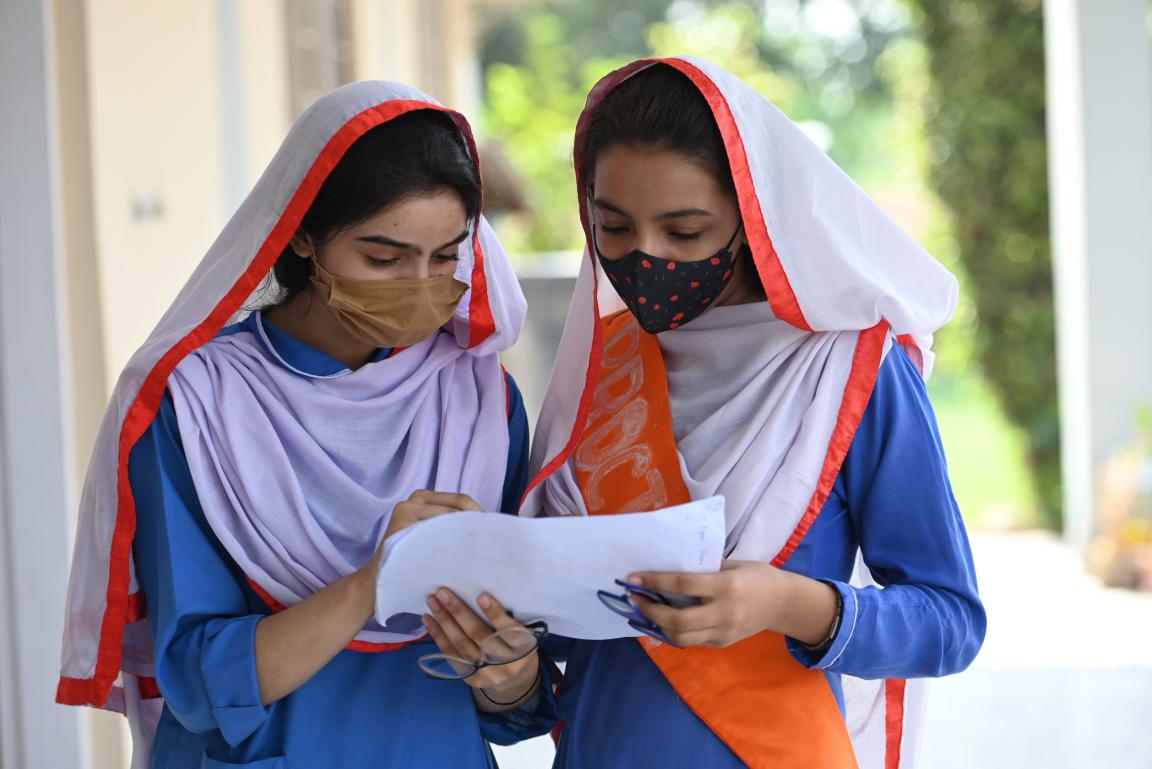 Two female students in school uniform reviewing schoolwork together.
