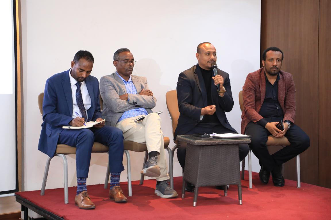 A group of panelists with one of them holding a mic and speaking 