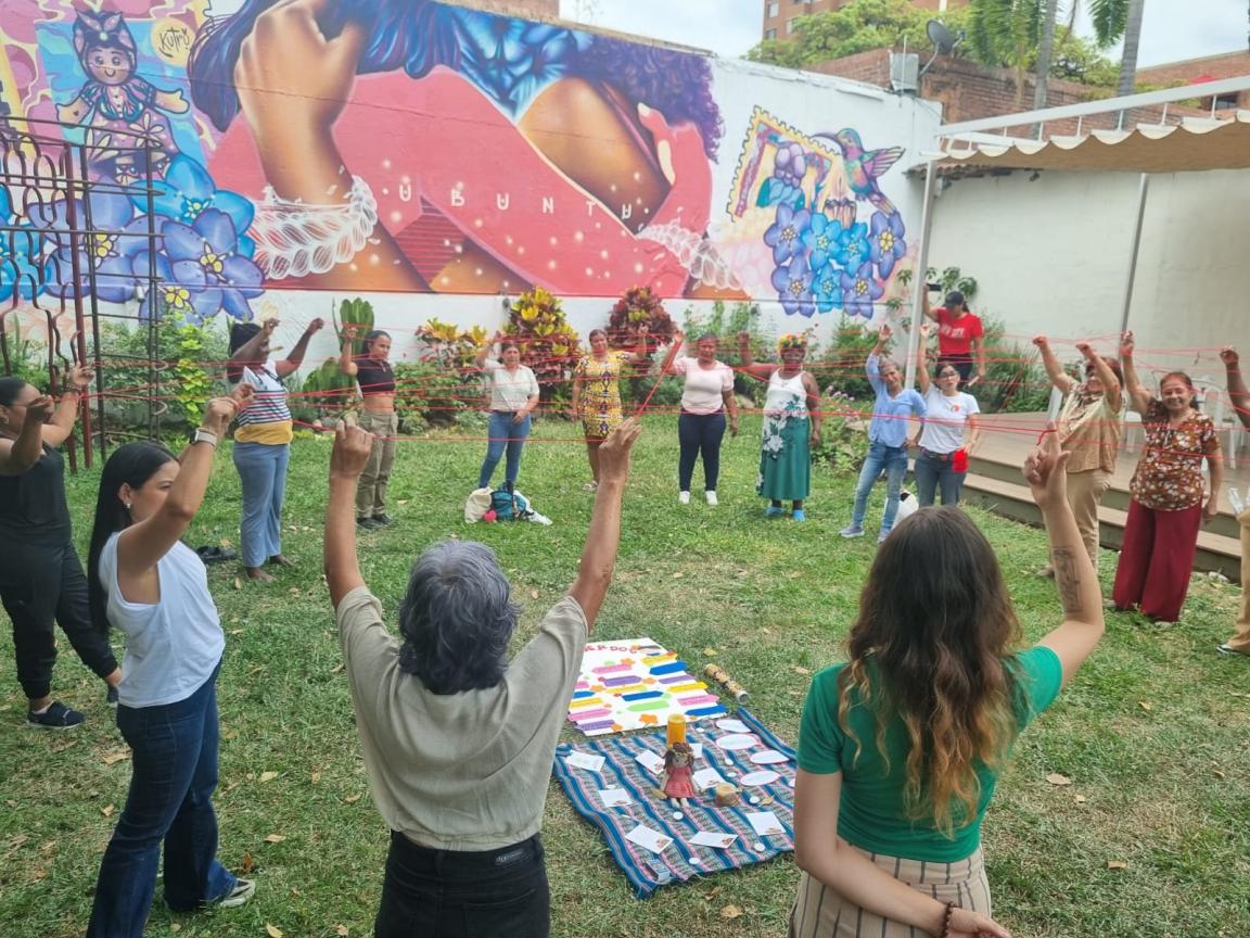 Un grupo de mujeres levantan las manos en un círculo de tejedoras.