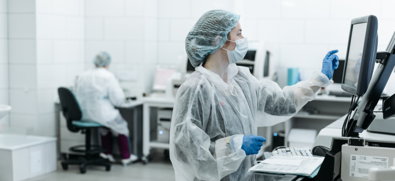 Eine Ärztin in Laborkleidung tippt auf einen Monitor.