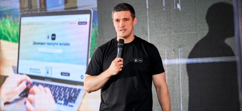 Ein Mann spricht in ein Mikrophon. Hinter ihm ist eine Präsentation zu Digitalisierung zu sehen.