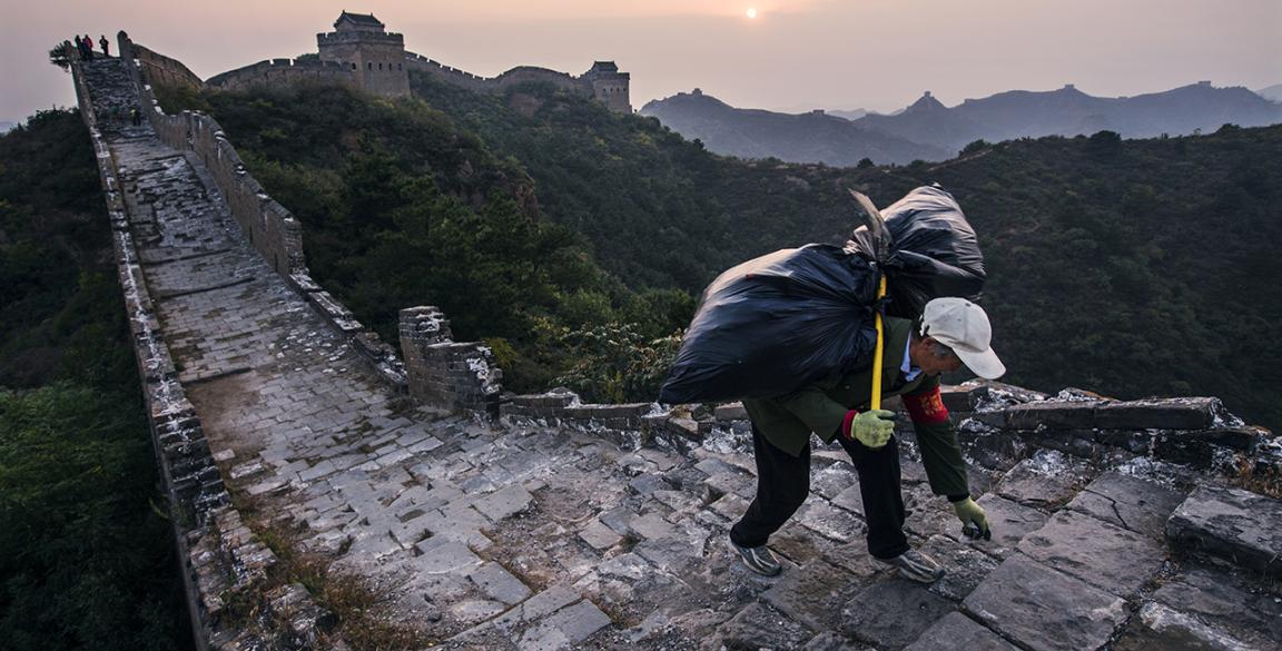 Ein Mann schleppt einen Sack auf seinem Rücken die Chinesische Mauer hoch