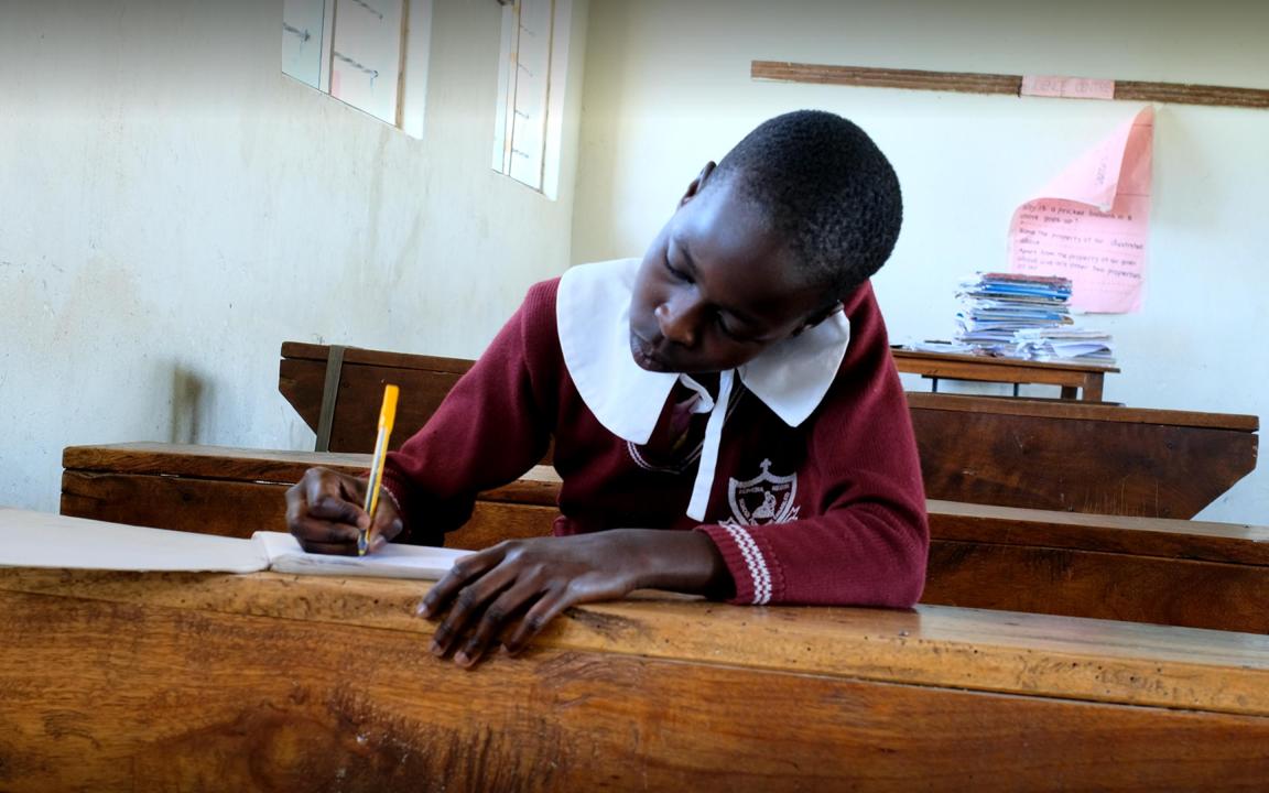 Mädchen sitzt auf einer Schulbank und schreibt in ein Heft
