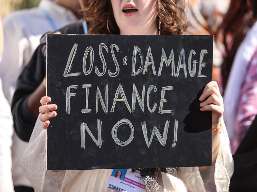Frau mit einem Schild auf dem steht "LOSS & DAMAGE FINANCE NOW!"