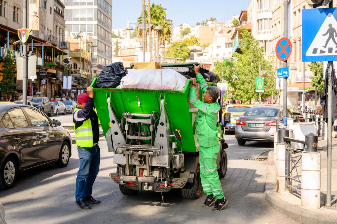 Men loading rubbish into a small rubbish truck