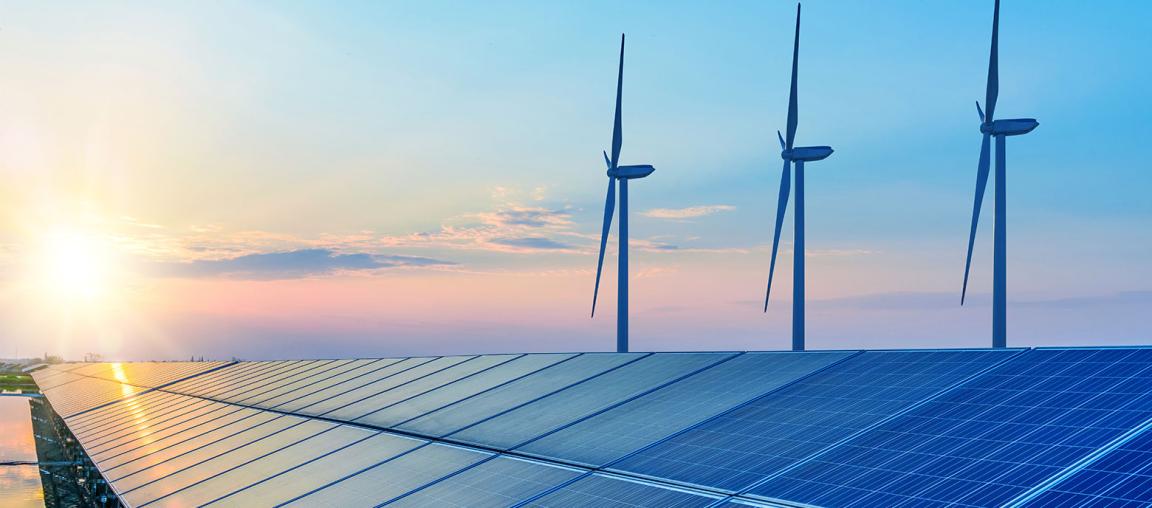 Eine Reihe von Solaranlagen im Vordergrund mit drei Windrädern dahinter, abgebildet vor einem Himmel in blauen und rosafarbenen Abendtönen.