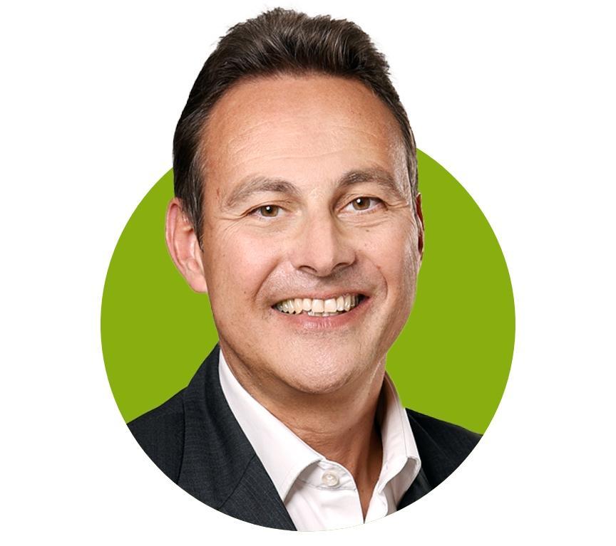 Portrait of a smiling man with short dark hair, wearing a white shirt and dark grey jacket, in front of a green circle on a white background.