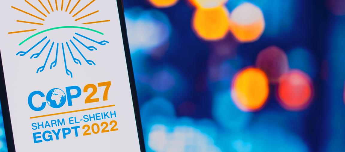 Ein Werbeplakat für die Klimakonferenz COP27 in Sharm El-Sheikh, Ägypten 2022. Das Design zeigt eine stilisierte Sonne in Orange und Grün über dem blauen Logo für COP27, darunter der Globus, und den Veranstaltungsort und das Jahr in Blau und Orange.
