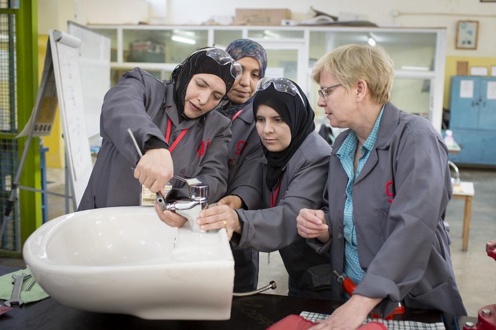 Drei Frauen schrauben an einem Wasserhahn. Eine weitere sieht zu.