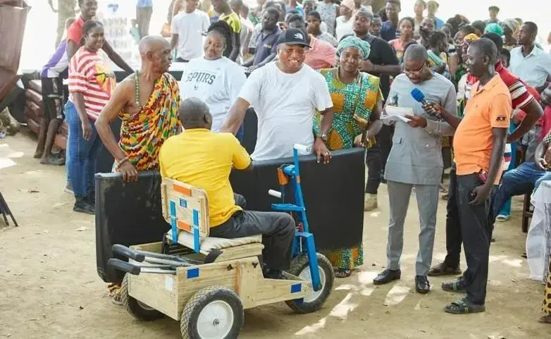 A man sitting in a wheelchair receives a mattress from smiling helpers.