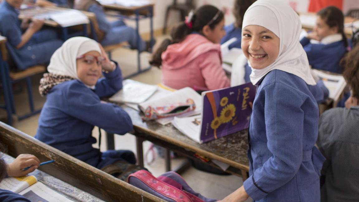 Mehrere Schülerinnen sitzen auf Schulbänken, auf den Tischen liegen Bücher. 