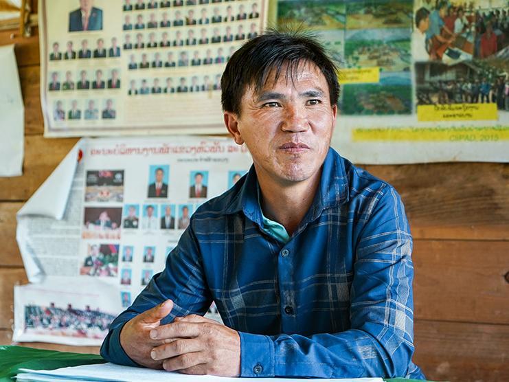 Ein Mann sitzt an einem Tisch, hinter ihm ist eine Holzwand mit Plakaten