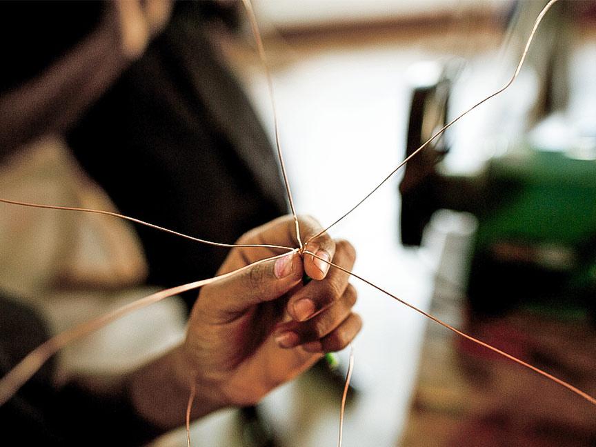 Close-up of a hand holding several thin copper wires and twisting them together.