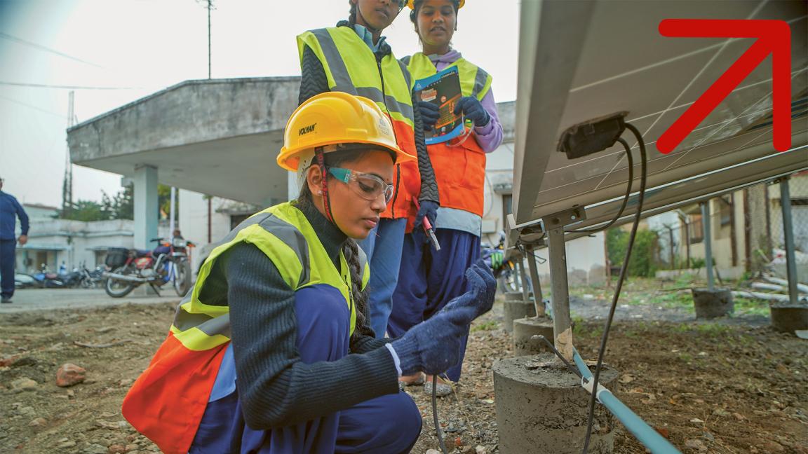 Eine Frau in Arbeitsbekleidung überprüft Kabelverbindungen eines Solarmoduls. 