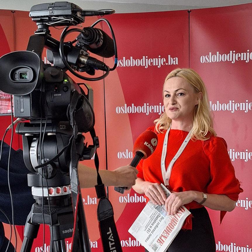 Eine Frau steht vor einer Kamera und spricht in ein Mikrofon.