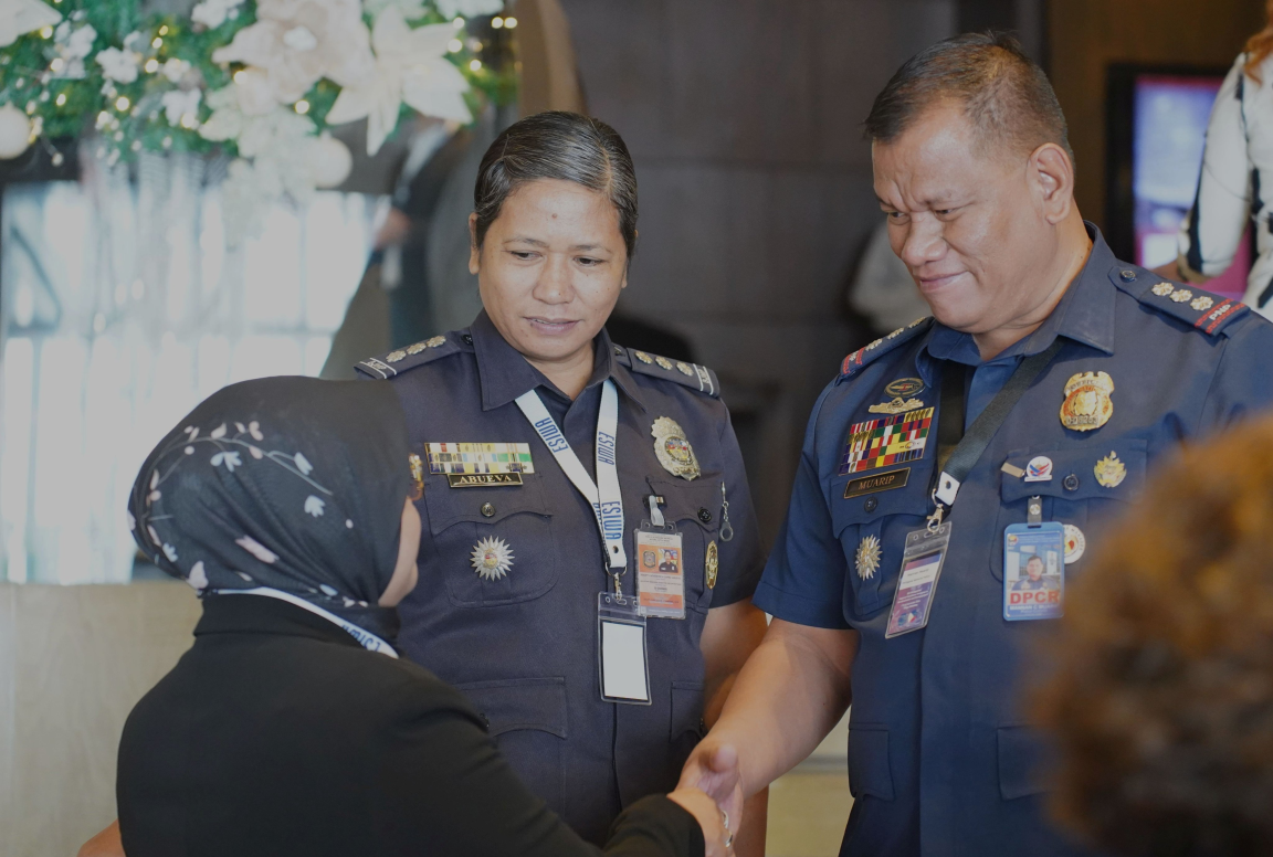 Ein Mann und eine Frau in blauer Militäruniform, der Mann schüttelt eine Frau mit Kopftuch lächelnd die Hand
