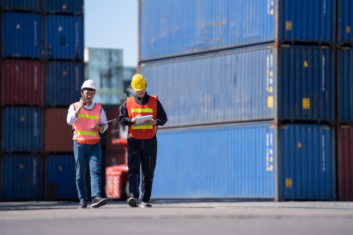 Zwei Männer laufen ein Hafengelände entlang.