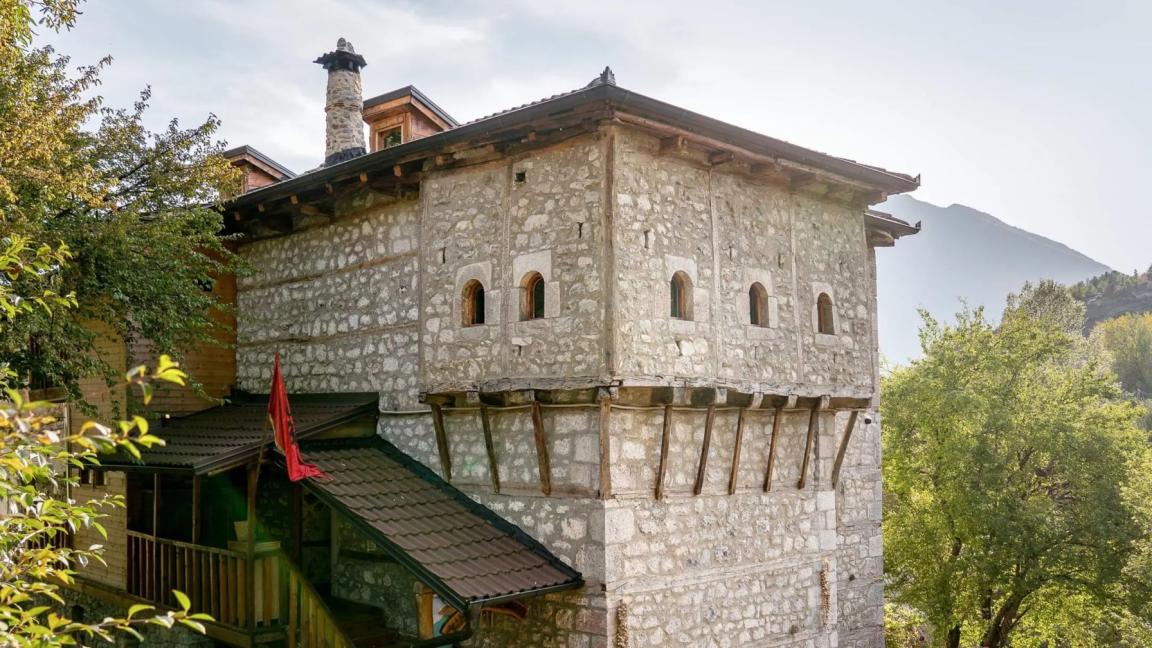 Ein historisches Steingebäude mit kleinen Fenstern und hölzernem Dach in grüner Umgebung.