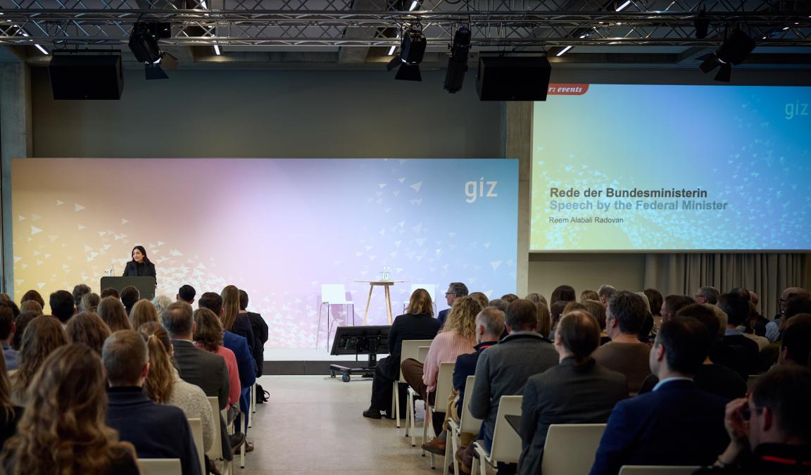 Many people sitting in a hall listen to the speech by the Federal Development Minister Reem Alabali Radovan