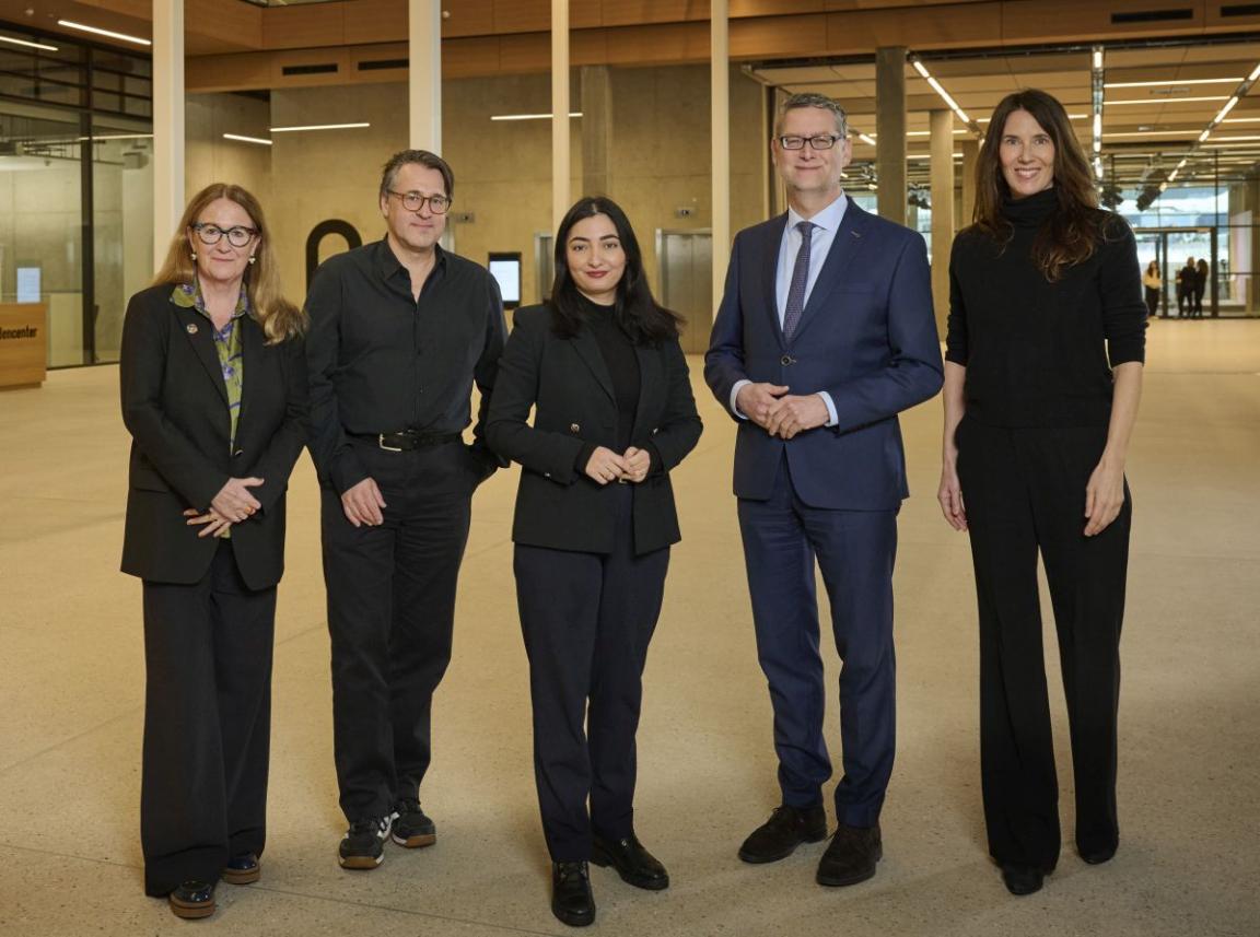 Five people in business attire are standing smiling in a large room.